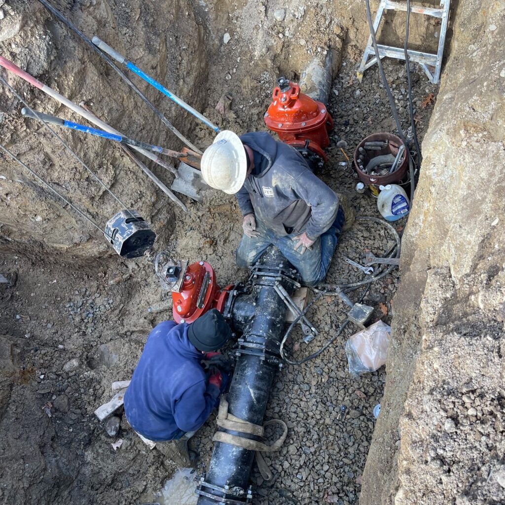 Crew installing valves on underground water main in trench